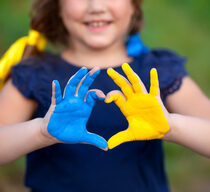 Kleines Mädchen zeigt Hände in Herzform, die in der ukrainischen Flaggenfarbe gemalt sind - gelb und blau.