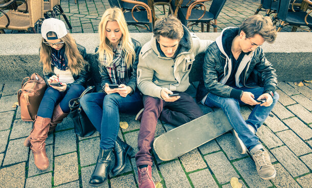 Jugendliche sitzen in Gruppe und spielen mit Smartphones