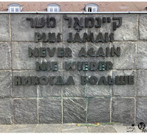 Schriftzug „Nie wieder” in fünf verschiedenen Sprachen, der an einer Steinmauer in der Gedenkstätte des ehemaligen KZ Dachau angebracht ist.