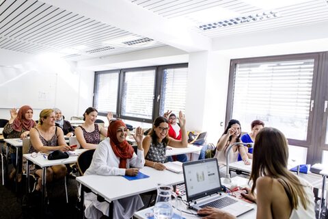 Eine Gruppe aus Frauen, darunter einige mit Kopftüchern, in einer Unterrichtsituation