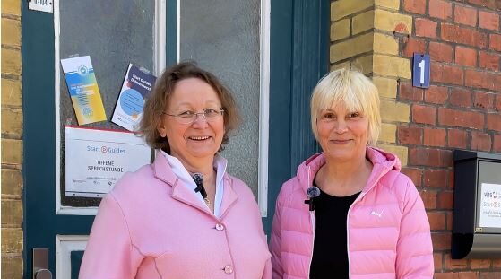 Zwei Frauen stehen vor einer Tür und gucken in die Kamera