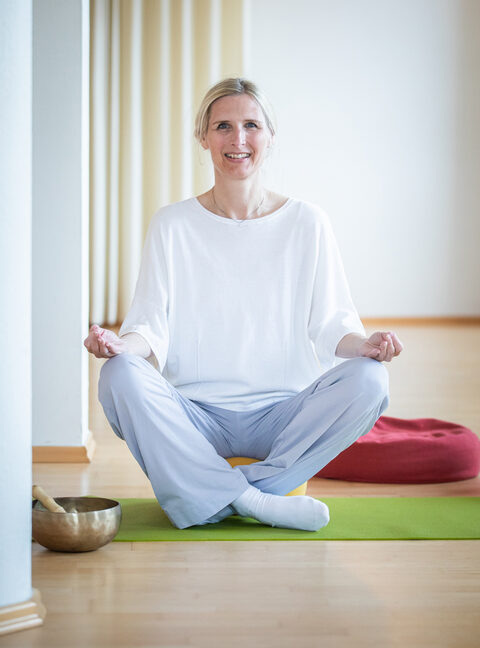 Eine Frau im Schneidersitz auf einer Yogamatte