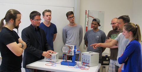 Eine Gruppe von jungen Männern und einer jungen Frau stehen um einen Tisch herum, auf dem elektrische Geräte aufgebaut sind.