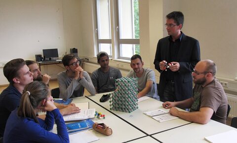 Eine Gruppe von jungen Männern und einer jungen Frau sitzen an einem Tisch, auf dem ein Bausatz von chemischen Molekülen aufgebaut ist.