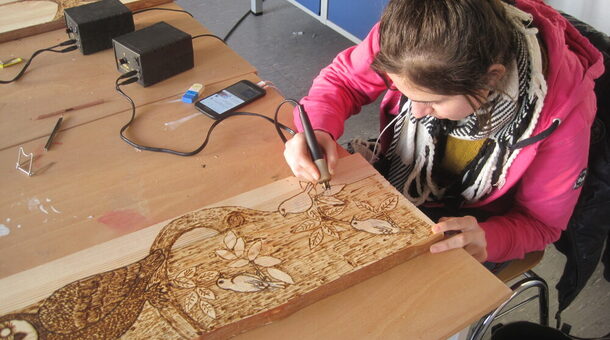 Eine Frau schnitzt ein Bild von Vögeln und einer Eule in ein Holzbrett