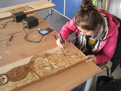 Eine Frau schnitzt ein Bild von Vögeln und einer Eule in ein Holzbrett