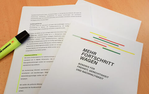 Auf einem Tisch liegt der Koalitionsvertrag "Mehr Fortschritt wagen" von SPD, Bündnis 90/ Die Grünen und FDP. Mit einem gelben Marker ist der Abschnitt "Erwachsenenbildung" gelb hervorgehoben.