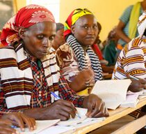 Afrikanische Erwachsene sitzen in einem Klassenzimmer und schreiben in Hefte
