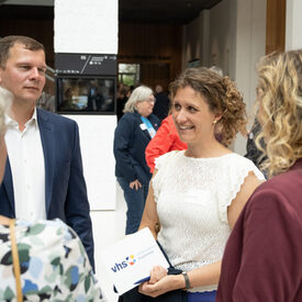 Eine lächelnde Frau steht in einer Gruppe und hält eine Karte mit vhs-Logo in den Händen.