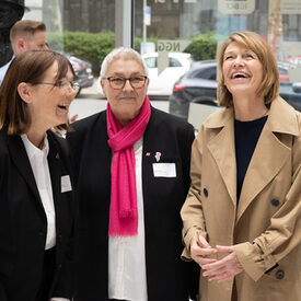 Drei Frauen stehen zusammen und lachen.