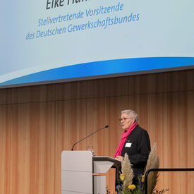 Eine Frau steht vor einem Redepult auf einer Bühne.