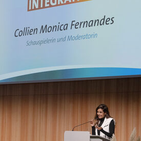 Eine Frau steht vor einem Redepult auf einer Bühne.