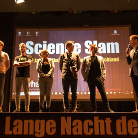 Die teilnehmenden des Science Slam stellen sich auf der Bühne dem Votum des Publikums.