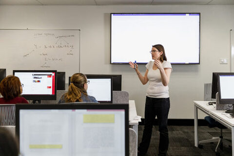 Dozentin unterrichtet in einem Computerraum vor einem digitalen Whiteboard