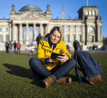 Frau sitzt auf der Wiese vor dem Deutschen Bundestag und blickt auf ihr Handy