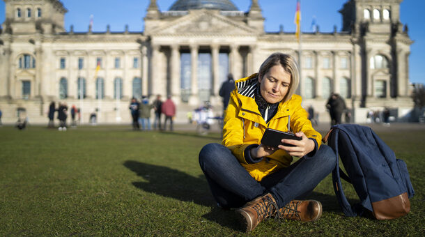 Frau sitzt auf der Wiese vor dem Deutschen Bundestag und blickt auf ihr Handy