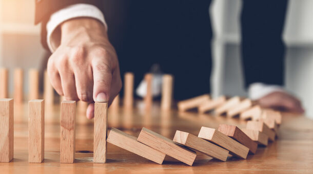 Close up finger businessman stopping wooden block from falling in the line of domino with risk concept.