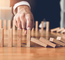 Close up finger businessman stopping wooden block from falling in the line of domino with risk concept.