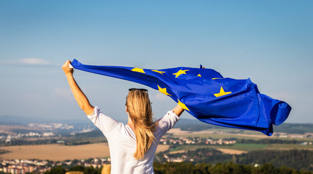 Frau steht mit wehender EU-Flagge vor Landschaft