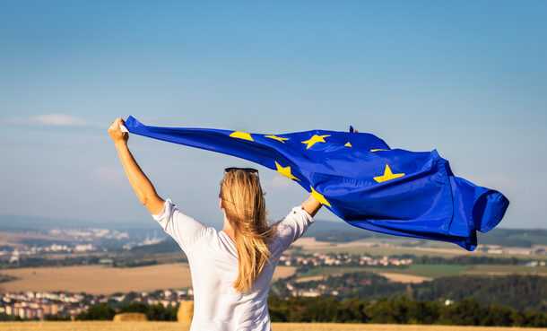 Frau steht mit wehender EU-Flagge vor Landschaft