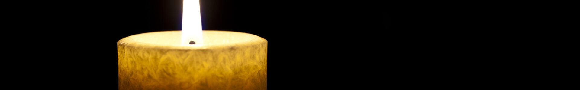Eine einzelne Kerze brennt vor dunklem Hintergrund