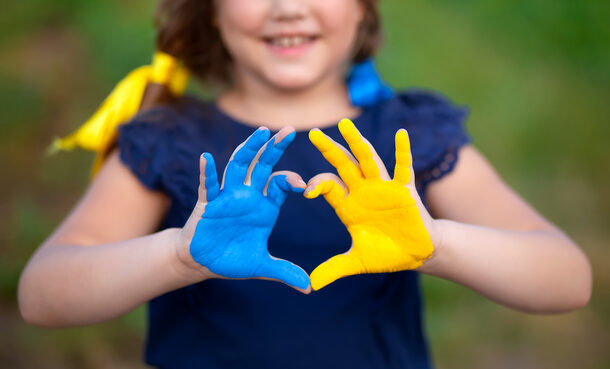 Kleines Mädchen zeigt Hände in Herzform, die in der ukrainischen Flaggenfarbe gemalt sind - gelb und blau.