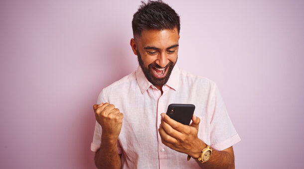 Junger Mann freut sich über Nachricht am Smartphone.