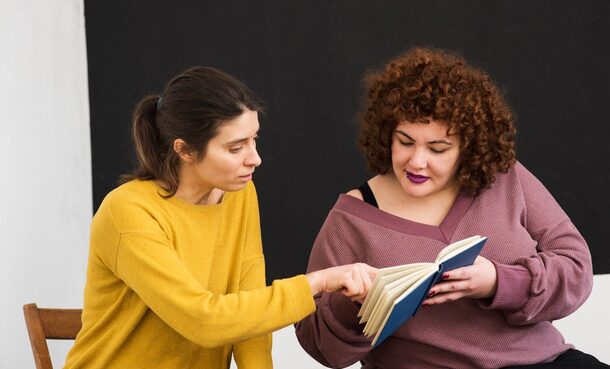 Eine Ehrenamtlerin hilft einer Frau beim Lesen lernen