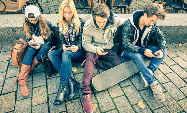Jugendliche sitzen in Gruppe und spielen mit Smartphones
