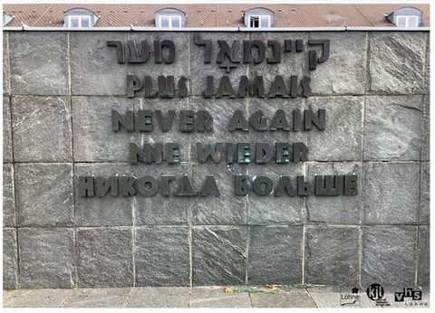 Schriftzug „Nie wieder” in fünf verschiedenen Sprachen, der an einer Steinmauer in der Gedenkstätte des ehemaligen KZ Dachau angebracht ist.