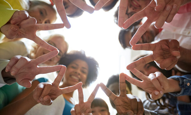 Junge Menschen bilden mit den Fingern Kreis aus Peace Zeichen.