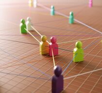 Symbolbild für Netzwerke: Bunte Holzfiguren in einem Raum sind durch Fäden miteinander verbunden