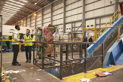 Warehouse manager and colleague talk by recycling machinery