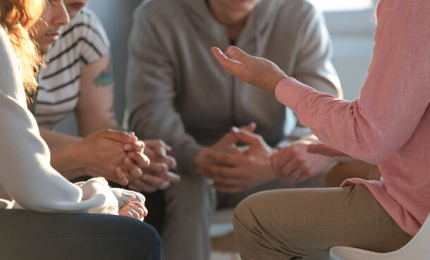 Close-up of a therapist gesticulating while talking to a group of listing teenagers during an educational self-acceptance and motivation meeting.