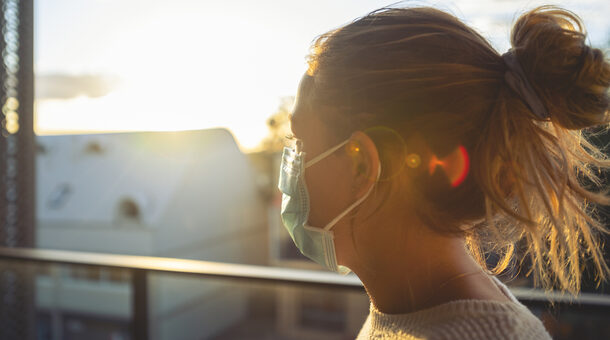 Junge Frau mit Maske guckt in den Sonnenuntergang
