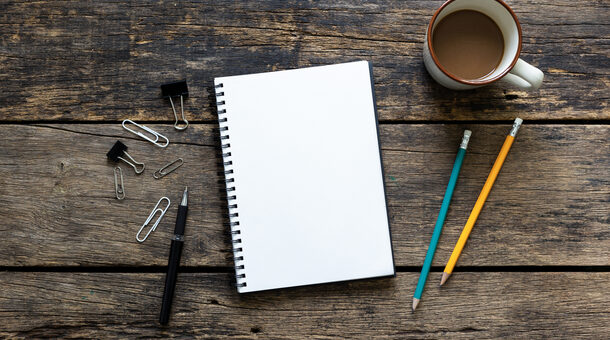 Notizbuch auf einem Tisch neben Stiften und Kaffeetasse