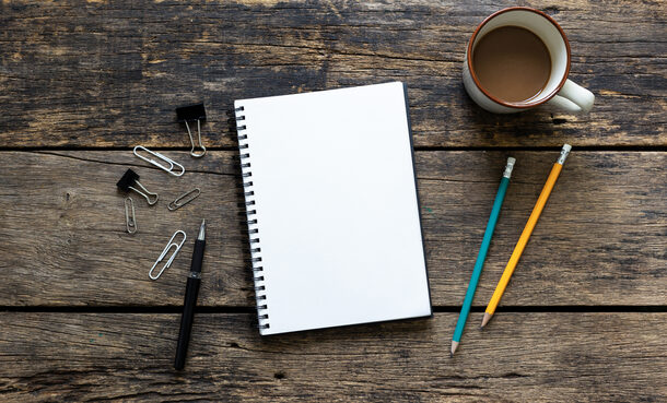 Notizbuch auf einem Tisch neben Stiften und Kaffeetasse