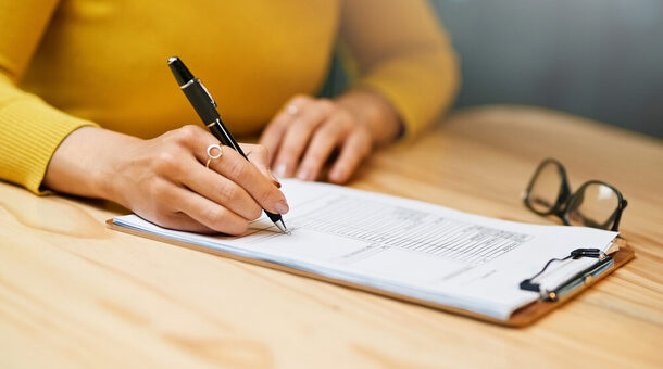 Eine Person füllt einen Antrag aus auf Papier mit einem Stift.