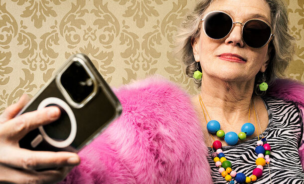 Eine ältere Frau bunt gekleidet mit Sonnenbrille und Smartphone in der Hand.