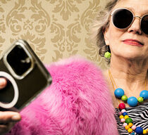 Eine ältere Frau bunt gekleidet mit Sonnenbrille und Smartphone in der Hand.