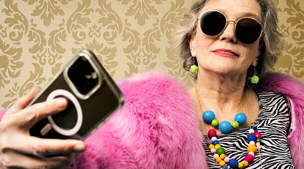 Eine ältere Frau bunt gekleidet mit Sonnenbrille und Smartphone in der Hand.