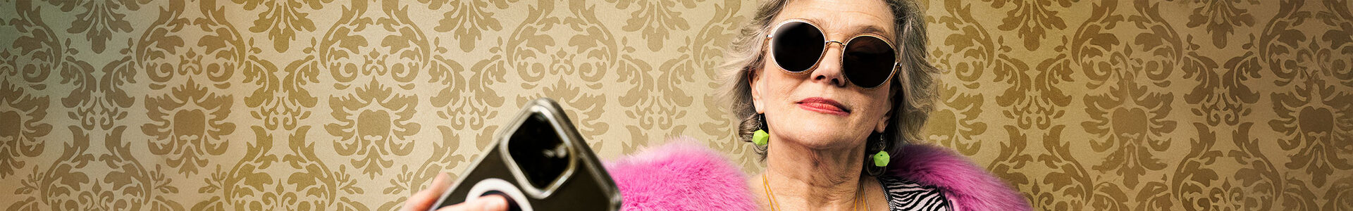 Eine ältere Frau bunt gekleidet mit Sonnenbrille und Smartphone in der Hand.