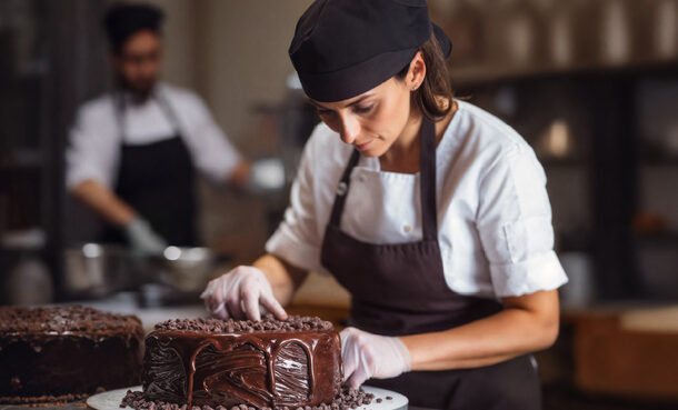 Eine jüngere Frau dekoriert eine Torte mit Schokoüberzug.