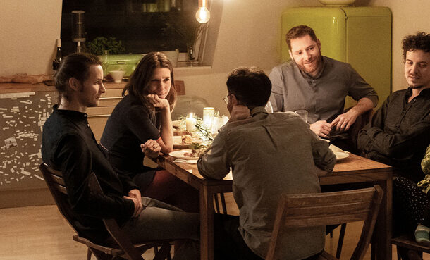 Blick in eine gemütliche Küche. Am Küchentisch sitzen mehrere Personen, die sich unterhalten.