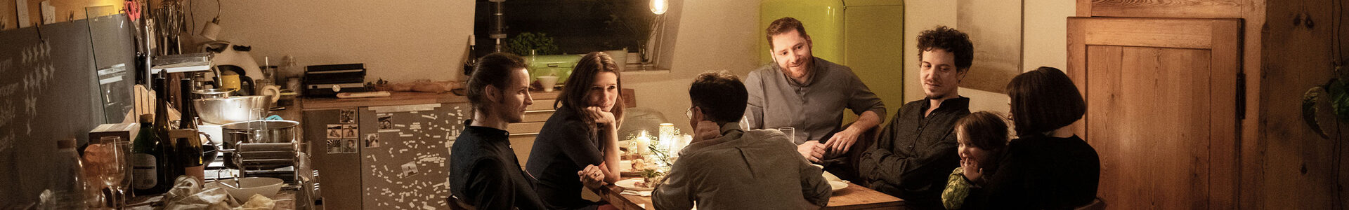 Blick in eine gemütliche Küche. Am Küchentisch sitzen mehrere Personen, die sich unterhalten.