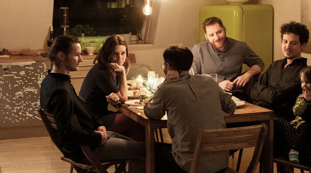 Blick in eine gemütliche Küche. Am Küchentisch sitzen mehrere Personen, die sich unterhalten.