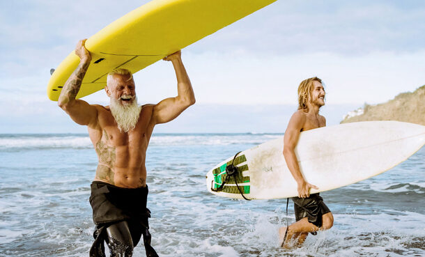 Ein älterer, durchtrainierter Mann und ein junger Mann kommen mit ihren Surfbrettern aus dem Meer.