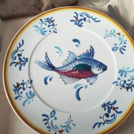 Eine Nahaufnahme eines mit einem Fisch und Ranken verzierten Keramikteller auf einem gedeckten Tisch.
