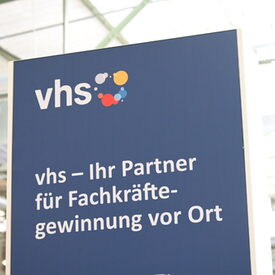 Bild des Roll-Ups am Stand des DVV. Weiße Schrift auf dunkelblauem Grund: vhs - Ihr Partner für die Fachkräftegewinnung vor Ort.