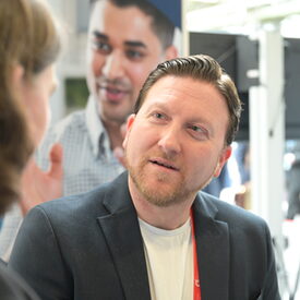 Ein männlicher Vertreter der vhs mittleren Alters in schwarzem Sakko im Gespräch mit einer Besucherin.